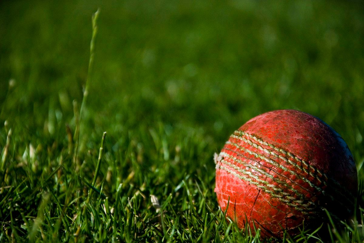 Red cricket ball resting on a grass field